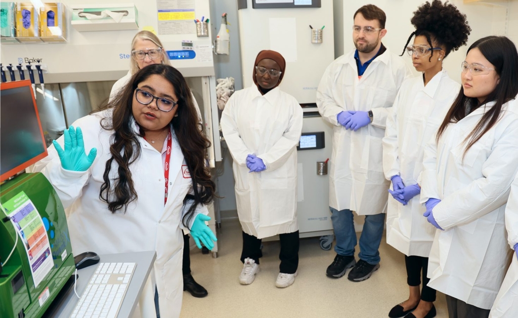 students in lab coats touring a lab with company representative