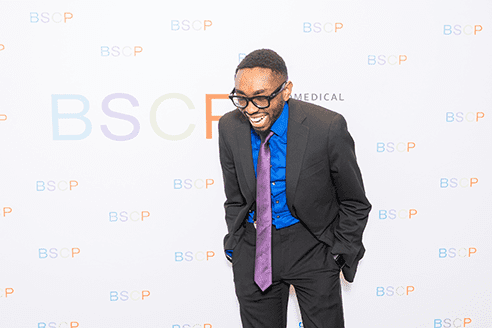 BSCP student leaning forward and laughing in front of BSCP step and repeat