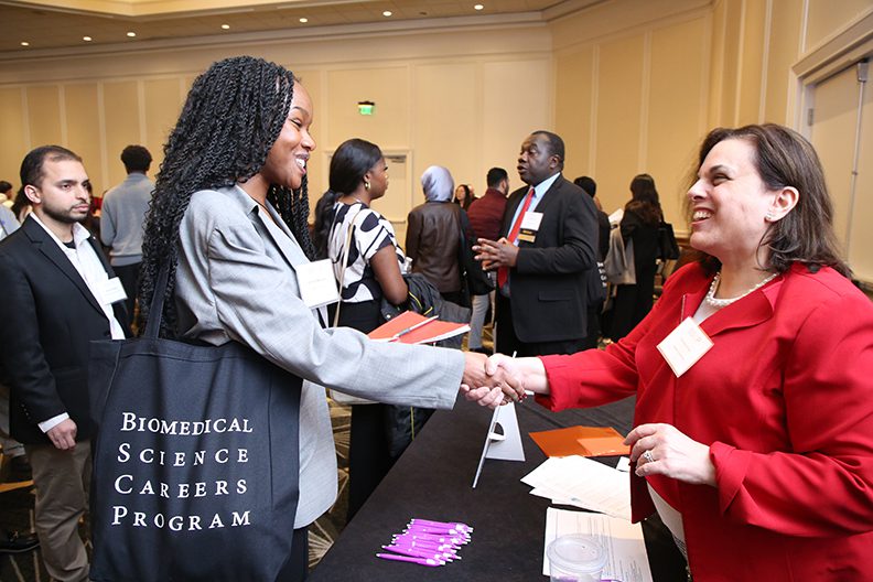 two women shaking hands over a table at a conference