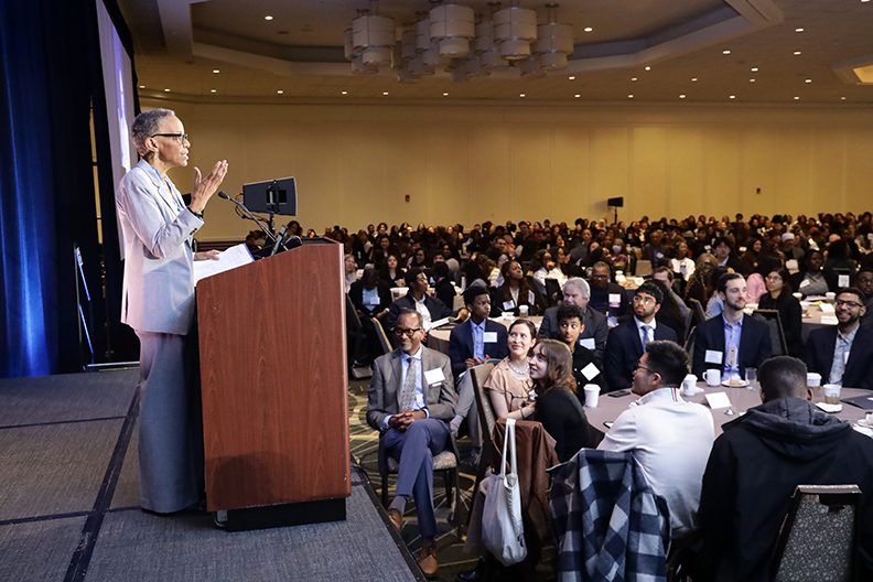 person at podium speaking in front of room full of conference attendees