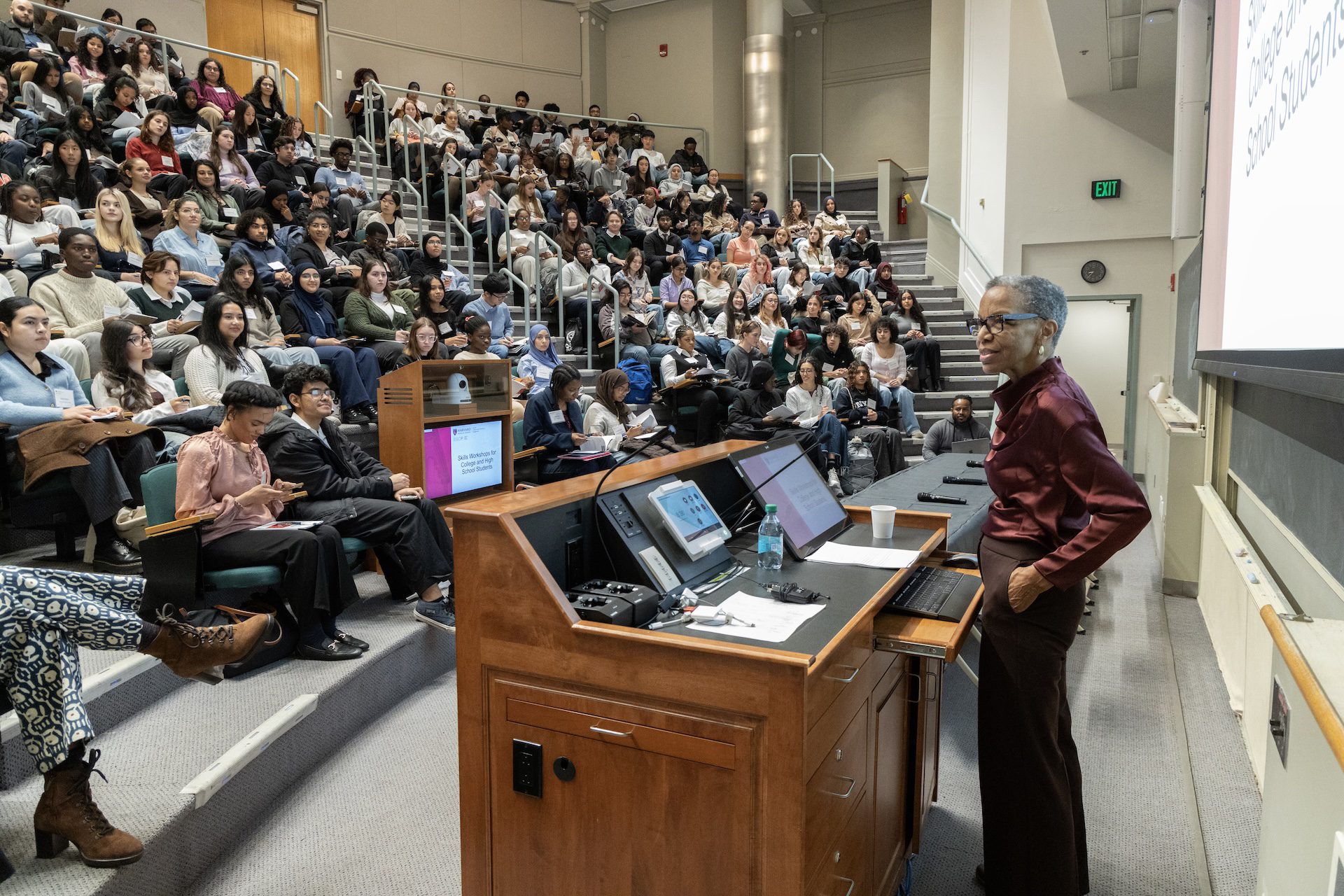 instructor in front of lecturn in lecture hall full of students