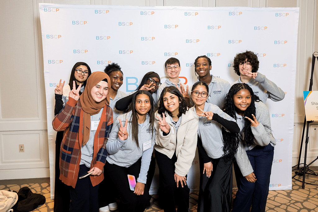 a group of young students showing the peace sign standing in front of a bscp step and repeat