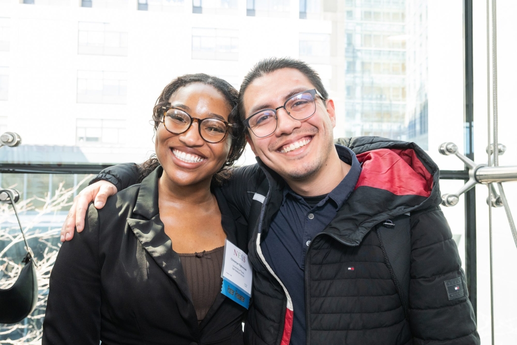 a woman and man leaning on each other arms around shoulders, smiling at camera