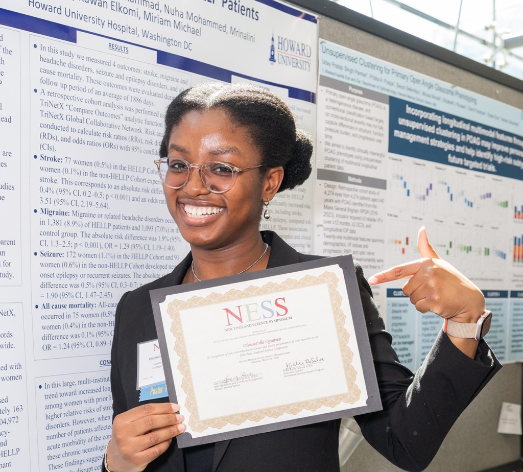 young woman holding NESS certificate pointing at it in front of poster presentation