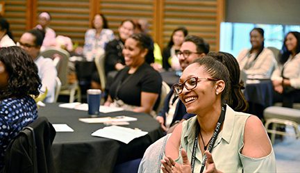 alumni conference, people sitting at roung tables, smiling woman in forefront