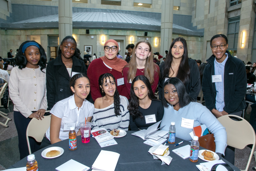 Group of students standing in two rows behind a round table at a luncheon